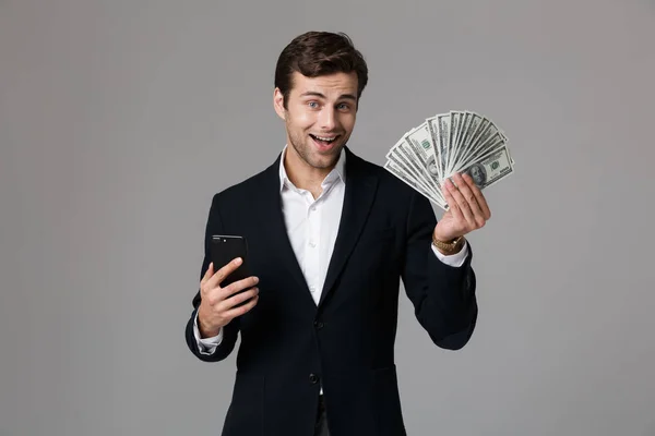 成功した実業家 代お金と灰色の背景上分離されたスマート フォンのファンを保持のスーツでのイメージ — ストック写真