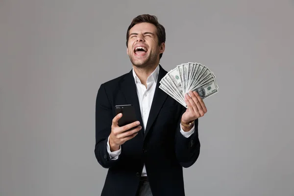 感情的な実業家 代お金と灰色の背景上分離されたスマート フォンのファンを保持のスーツでのイメージ — ストック写真