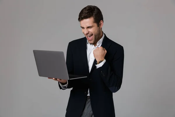 スーツは 灰色の背景の上分離されたノート パソコンを使用しながら歓喜の恍惚としたビジネスマン 代のイメージ — ストック写真