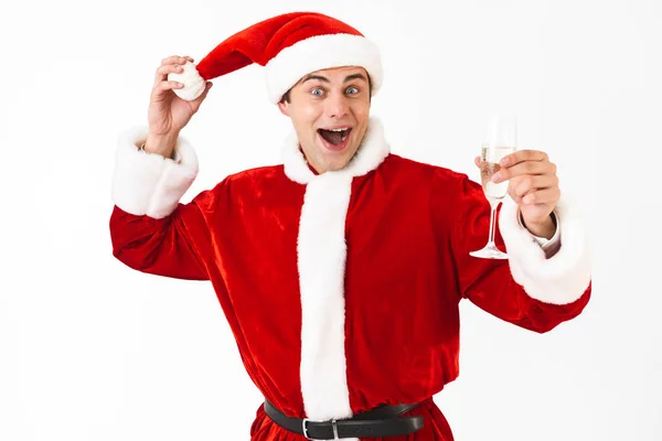 幸福的人30多岁的肖像在圣诞老人服装和红色帽子喝香槟酒从玻璃查出在白色背景在演播室 图库图片