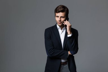 Cep telefonuyla konuşurken gri duvar arka plan üzerinde izole bir yakışıklı genç iş adamı görüntüsü.