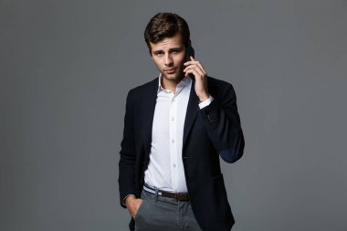 Cep telefonuyla konuşurken gri duvar arka plan üzerinde izole bir yakışıklı genç iş adamı görüntüsü.