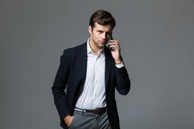 Cep telefonuyla konuşurken gri duvar arka plan üzerinde izole bir yakışıklı genç iş adamı görüntüsü.