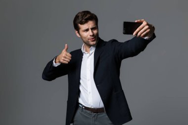 Kendine güvenen genç işadamı portresi bir selfie alarak, gri arka plan üzerinde izole takım elbise giymiş