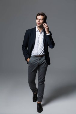 Yürüme, gri arka plan üzerinde izole uymak cep telefonu üzerinde mutlu bir genç işadamı portresi tam uzunlukta giymiş