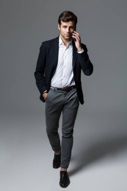 Yürüme, gri arka plan üzerinde izole uymak cep telefonunda bir kendine güvenen genç işadamı portresi tam uzunlukta giymiş