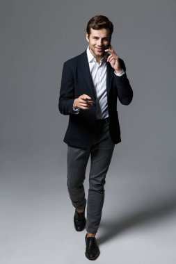 Yürüme, gri arka plan üzerinde izole uymak cep telefonu üzerinde mutlu bir genç işadamı portresi tam uzunlukta giymiş