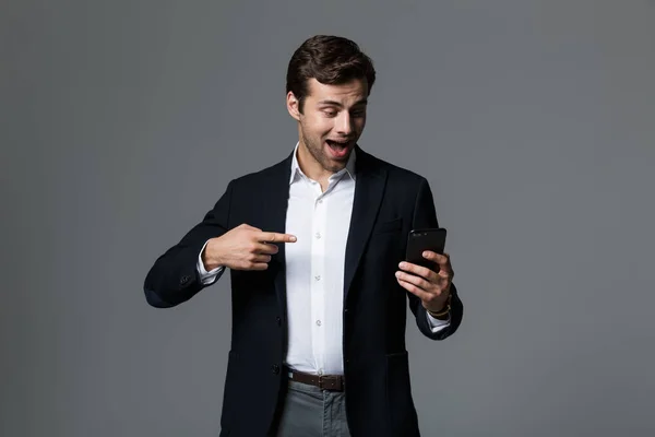 一个快乐的年轻商人的肖像 穿着西装孤立在灰色背景 指指点点手机 — 图库照片