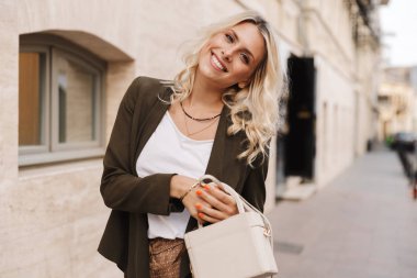 Çekici kadın 20'li yaşlarda holding çanta ve şehirde sokakta yürürken gülümseyen görüntüsü