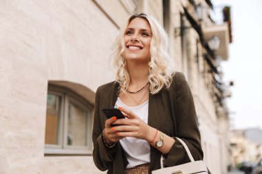 Şehirde sokakta yürürken sohbet için cep telefonu kullanarak ceket giyen beyaz kadın görüntüsünü