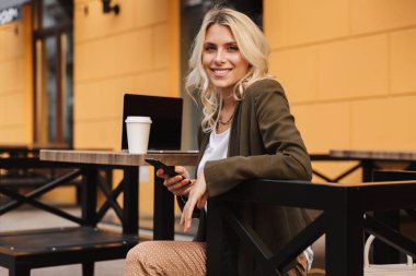 Paket servisi olan restoran kahve ve gümüş laptop ile açık kafede otururken güzel kadın 20'li yaşlarda holding cep telefonu portresi