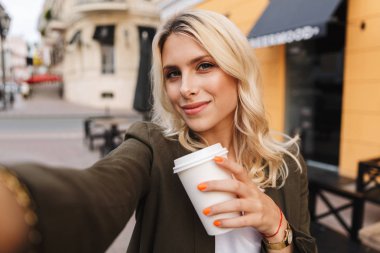 Kağıt bardak ve alma selfie paket servisi olan restoran kahve şehir sokak yürürken tutan memnun kadın görüntüsünü