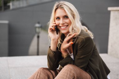 Çekici kadın 20'li yaşlarda görüntüsünü beton parapet açık otururken Smartphone'da konuşuyor