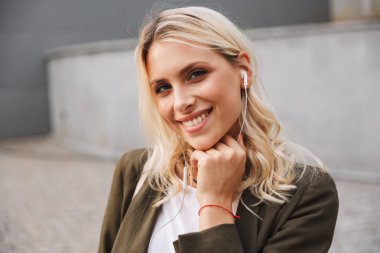 Görüntü kamera duran beton duvar açık boyunca gülümseyen güzel kadın 20'li yaşlarda giyen kulaklık