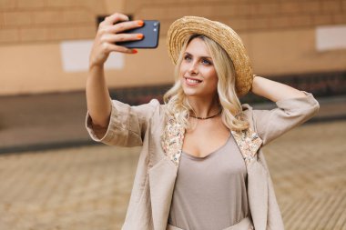 Zarif Bayan takım ve hasır şapka selfie şehir merkezinde açık fotoğraf çekerken gülümseyen görüntüsünü