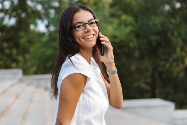 Açık havada cep telefonuyla konuşan yürüyen bir güzel iş kadın görüntüsünü.