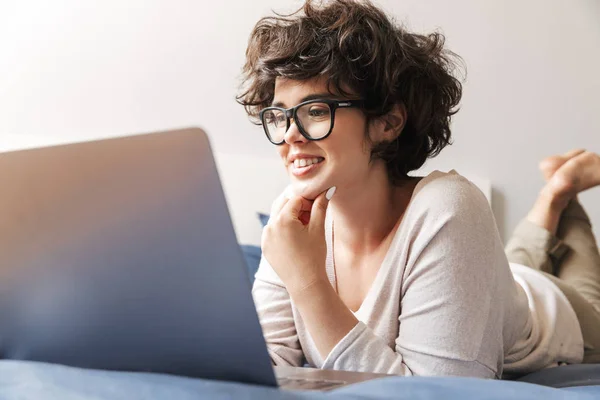 Image Happy Young Woman Lies Indoors Bed Using Laptop Computer — Stock Photo, Image