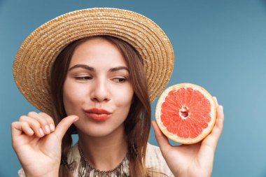 Narenciye giyen şapka tutan mavi duvardan izole mutlu genç heyecanlı güzel bir kadın görüntüsü.