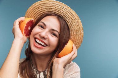 Narenciye giyen şapka tutan mavi duvardan izole mutlu genç heyecanlı güzel bir kadın görüntüsü.