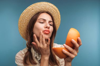 Görüntü izole mavi duvar arka plan ile portakal narenciye elinde bir ayna üzerinde ciddi bir güzel kadının poz.