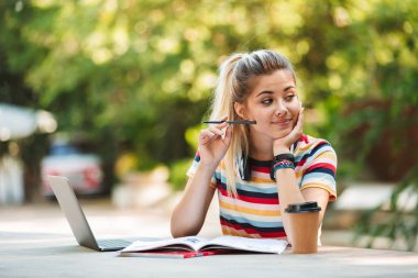 Görüntü dizüstü bilgisayar yazılı notları kullanarak parkta oturan bir düşünme düşünceli genç Sevimli kız öğrenci.