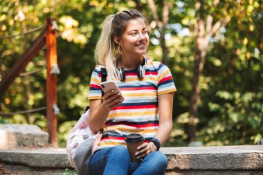 Mutlu sevimli genç kız kahve tutan cep telefonuyla görüntü.