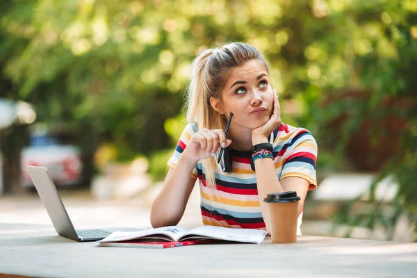 Görüntü dizüstü bilgisayar yazılı notları kullanarak parkta oturan bir düşünme düşünceli genç Sevimli kız öğrenci.