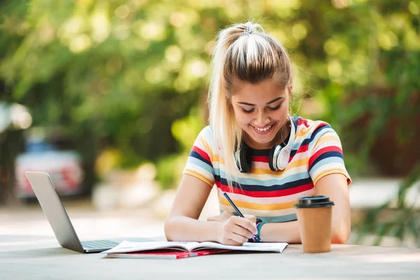 Görüntü dizüstü bilgisayar yazılı notları kullanarak parkta oturan bir mutlu genç Sevimli kız öğrenci.