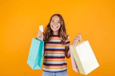 Holding alışveriş torbaları ve kredi kartı sarı duvar arka plan üzerinde poz mutlu bir genç kızın görüntü.