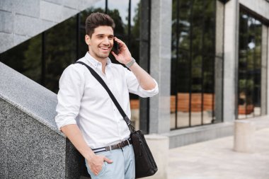 Başarılı genç işadamı gülümseyen beyaz gömlek açık havada, cep telefonu üzerinde konuşurken yürüyüş giyinmiş