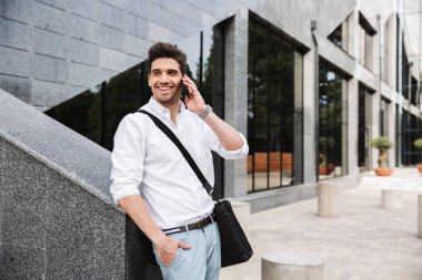 Başarılı genç işadamı gülümseyen beyaz gömlek açık havada, cep telefonu üzerinde konuşurken yürüyüş giyinmiş