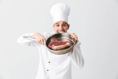 Beyaz arka plan üzerinde izole bir ham sığır eti biftek ile Tekdüzen gösteren kızartma tavası giyen neşeli Şef aşçı