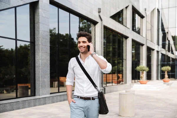 微笑着的成功的年轻商人穿着白衬衫走在户外 用手机说话 — 图库照片