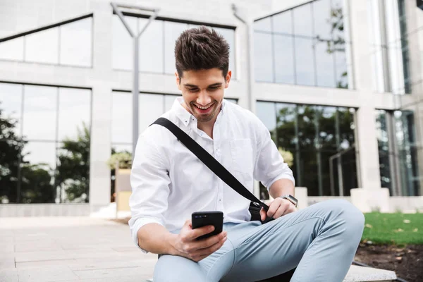 Başarılı genç işadamı gülümseyen beyaz gömlek açık havada, cep telefonu üzerinde konuşurken oturan giymiş