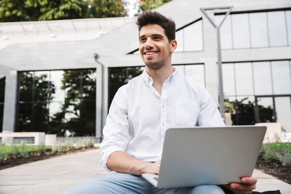 屋外に座ってラップトップ コンピューターで作業する若いビジネス人の笑顔 — ストック写真