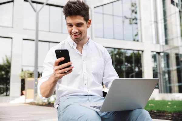 Boldog Fiatal Üzletember Szabadban Ülve Laptop Számítógép Mobiltelefon Használata — Stock Fotó