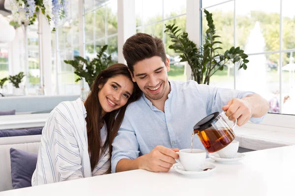お茶を飲んで カフェのテーブルに座っている若いカップルの笑顔 — ストック写真