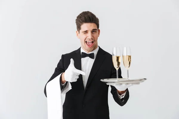 一个穿着燕尾服的微笑的年轻服务员的肖像为您提供了一杯香槟在白色背景 — 图库照片
