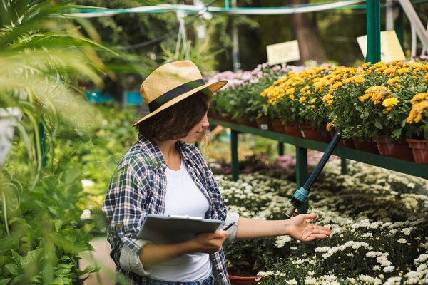 Pretty young woman working in a greenhouse, writing notes in a tablet