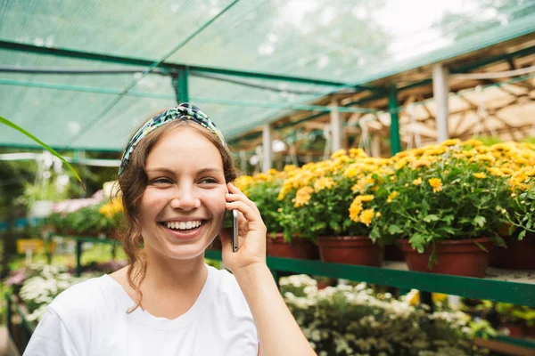 温室の中に立っている間携帯電話で話している陽気な若い女性庭師 — ストック写真
