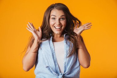 Excited young woman standing isolated over yellow background, celebrating success clipart
