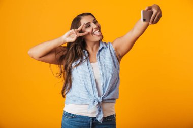 Bir selfie outsretched el ile alarak izole sarı arka plan üzerinde duran neşeli genç kadın