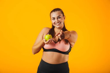 Sportif sutyen elma izole sarı arka plan üzerinde tutarak sağlıklı tombul kadın portresi