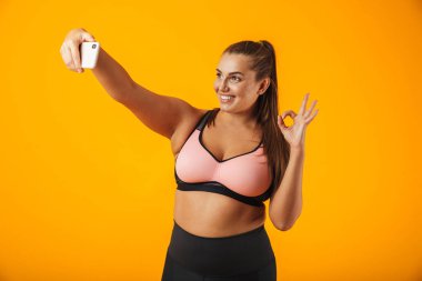 Sportif sutyen sarı arka plan izole selfie fotoğraf için cep telefonunuzun mutlu tombul kadın portresi