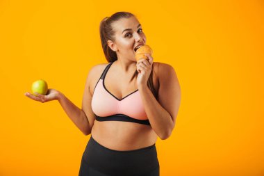 Elma tutan ve sarı arka plan üzerinde izole kruvasan yemek eşofman çok tombul kadın görüntüsünü