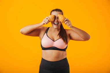 Resim iki ay çöreği izole sarı arka plan üzerinde her iki elinde tutan eşofman içinde neşeli tombul kadın