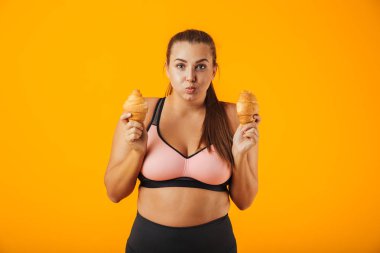 Resim iki ay çöreği izole sarı arka plan üzerinde her iki elinde tutan eşofman içinde eğlenceli tombul kadın