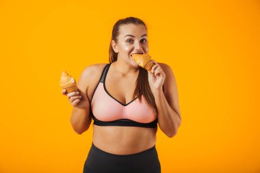 Görüntü üzerinde sarı arka plan izole kruvasan yemek eşofman içinde genç tombul kadın