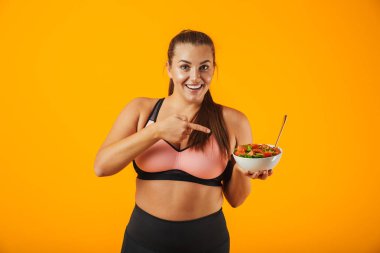 Görüntü kilolu kadının 20'li yeşil salata sarı arka plan üzerinde izole ile plaka tutarak eşofman