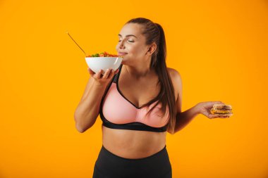 Görüntü plaka üzerinde sarı arka plan izole yeşil salata yemek eşofman içinde memnun tombul kadın